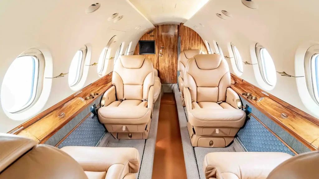 Air charter service interior with spacious tan leather seats and wood panel accents.