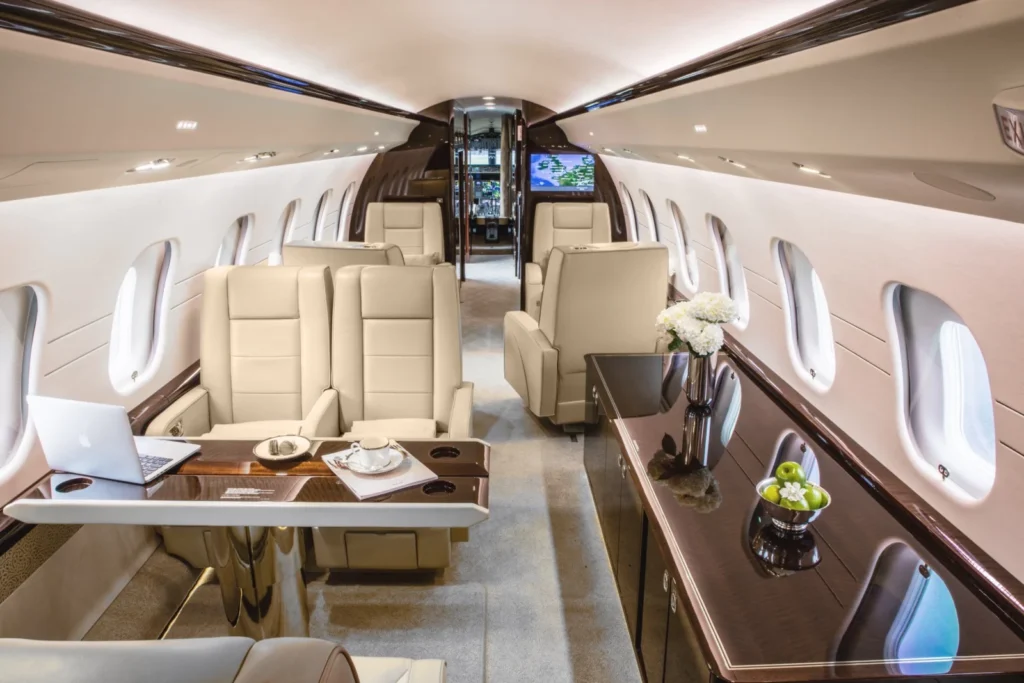 Elegant private jet interior with beige seating, workspace, and flower arrangements.