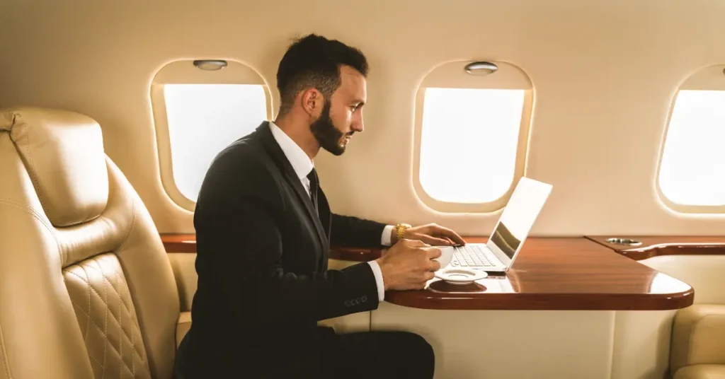 Cheap private jet flight experience with a man working on a laptop while enjoying coffee mid-flight.