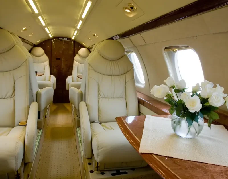 Executive jet charter interior with cream leather seats and fresh white roses on a polished wood table.