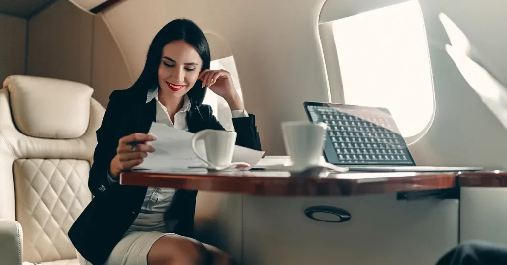 Jet charter service with a businesswoman reviewing documents on a private jet with a laptop and coffee.