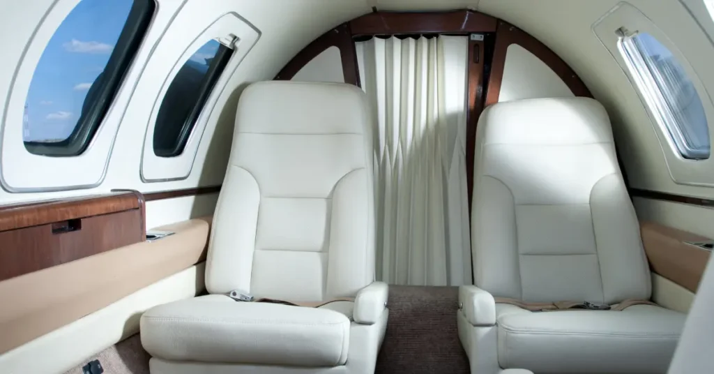 Luxury air travel cabin featuring two white leather seats and oval windows on a private jet.