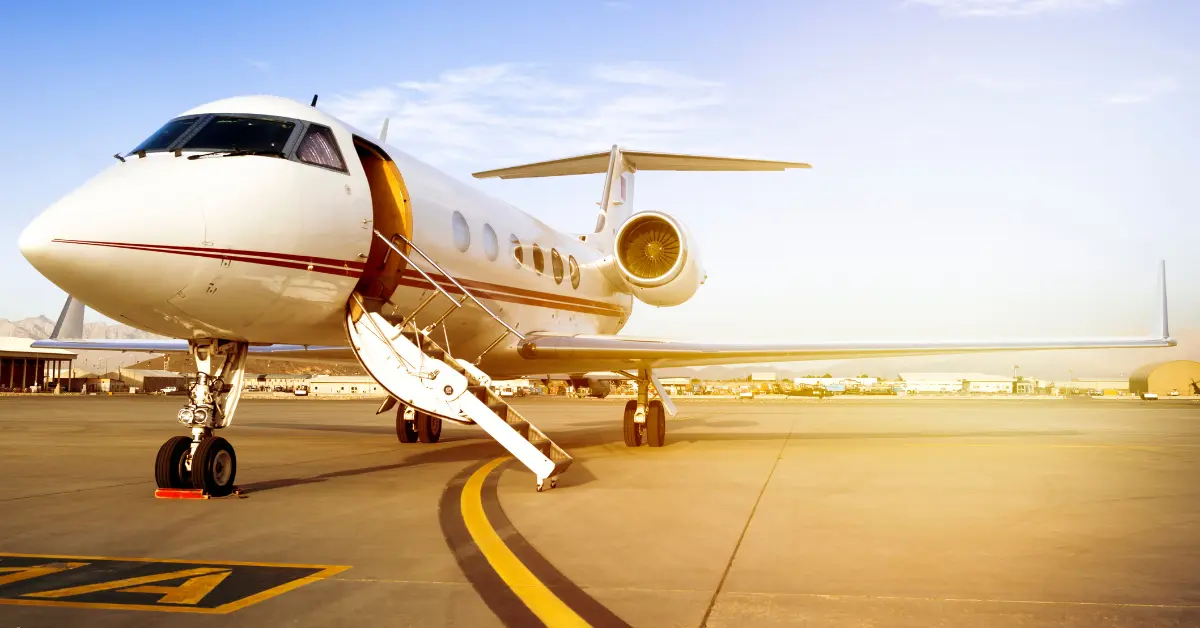 Private plane rental jet with stairway extended, ready for passenger boarding at sunny airport.
