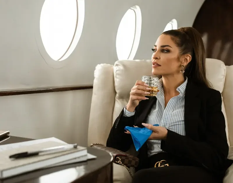 Private air travel with a woman sipping a drink in a plush seat aboard a business jet.