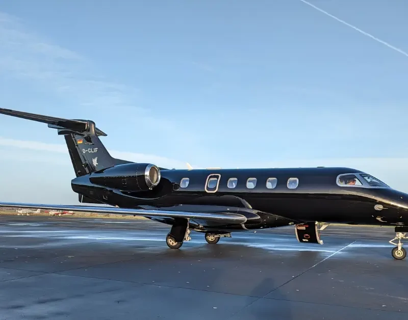 Private jet air charter aircraft parked on runway under clear blue sky.