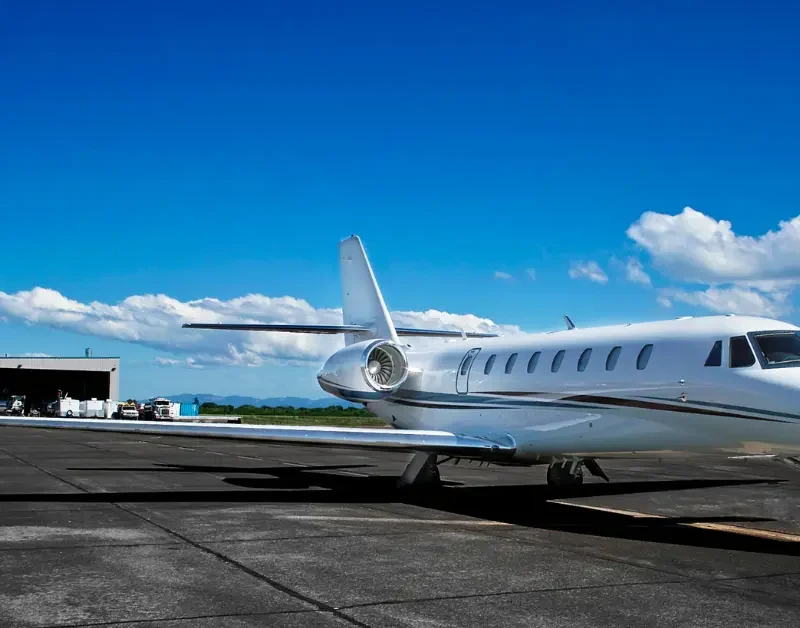 Private charter jet parked on a sunny tarmac near a hangar under a clear blue sky.
