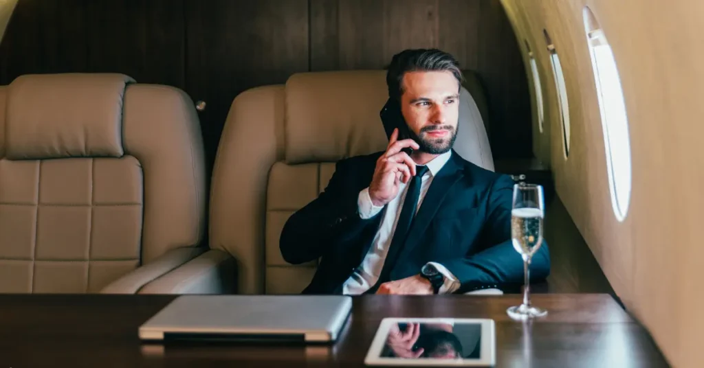 Private jet booking shown with businessman enjoying a call and champagne in luxurious cabin.