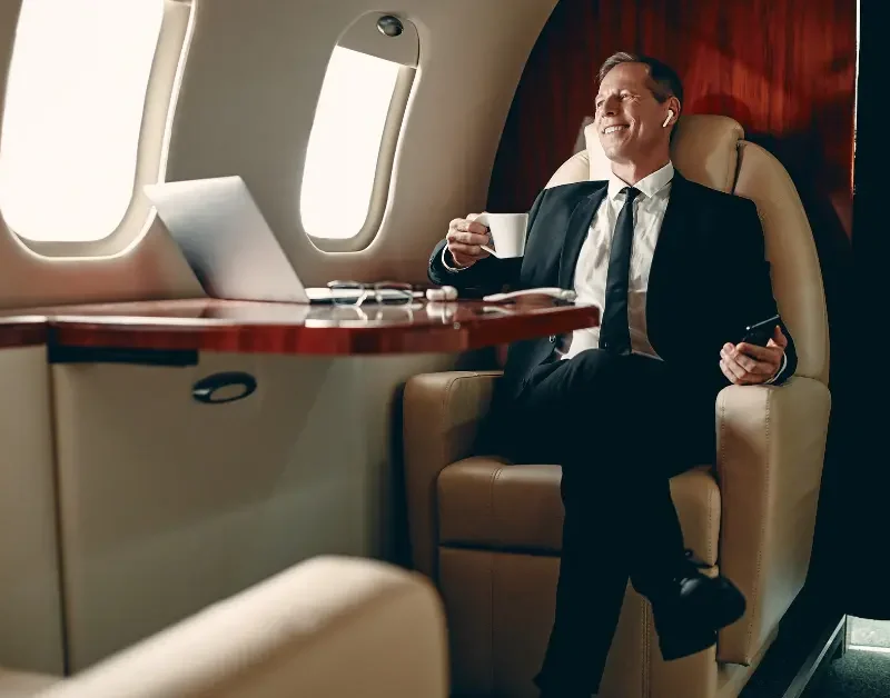 Private jet concierge service shown with business traveler enjoying coffee and working in-flight.